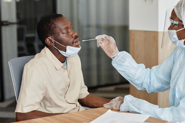 Homme noir ouvrant la bouche pour laisser le médecin prélever un écouvillon nasal pour prélever un échantillon pour le test de covid