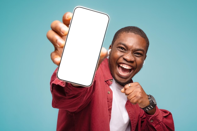 homme noir pointant sur un téléphone portable avec un écran blanc vide sur fond de studio bleu