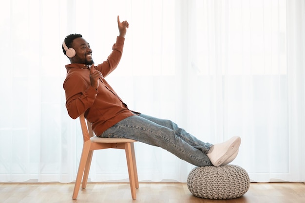 Homme noir portant des écouteurs écoutant de la musique assis à la maison