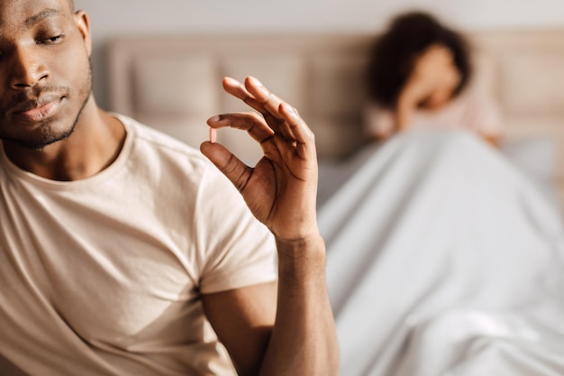 Photo homme noir prenant une pilule de puissance assis dans le lit avec sa petite amie
