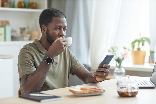 Un homme noir qui utilise un smartphone à la table de la cuisine
