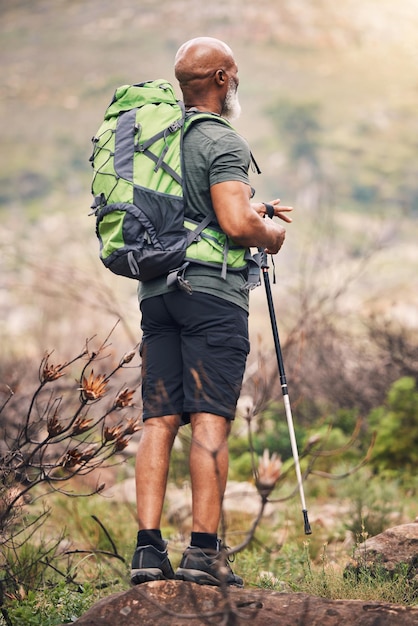 Homme noir randonnée et montagne avec sac à dos pour l'aventure de voyage ou le trekking dans la nature Randonneur afro-américain avec bâton debout sur un rocher pour voyager ou faire de la randonnée en plein air