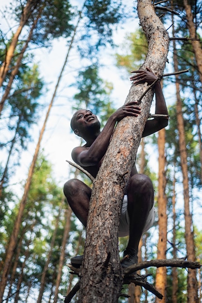 Homme noir sans chemise grimpe à un arbre