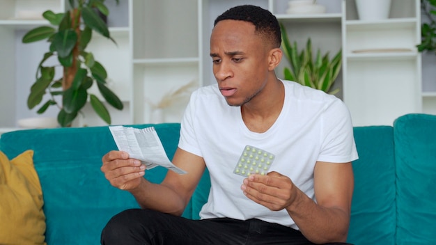 Homme noir seul assis sur le canapé des instructions de lecture malades comment prendre des pilules concentrées