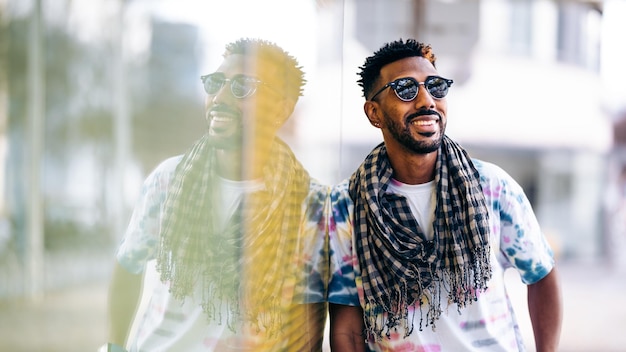 Homme noir souriant appuyé contre un mur de verre