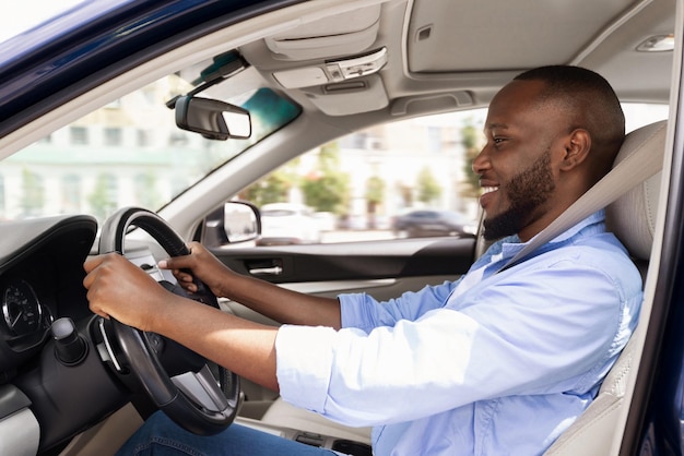 Homme noir souriant conduisant une nouvelle voiture en ville