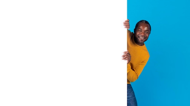 Photo homme noir souriant posant à côté d'un panneau publicitaire vierge
