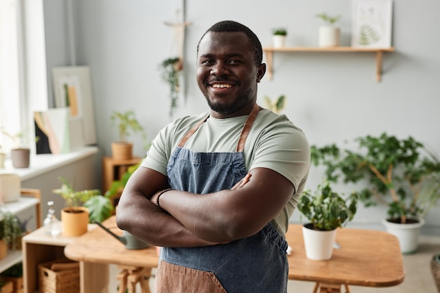 Homme noir souriant en tant que jardinier posant avec de la verdure à l'intérieur et regardant la caméra