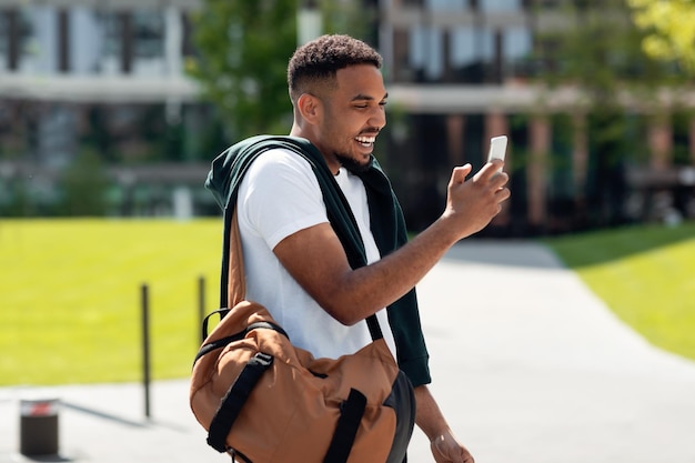 Homme noir souriant utilisant un téléphone marchant dans la ville