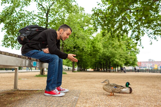 Un homme nourrit un canard de ses mains dans un parc de la ville. Le canard drôle se réjouit.