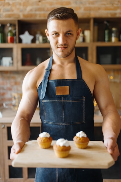 Un Homme Nu En Tablier Tient Un Plateau Avec Un Dessert Sucré Dans La Cuisine. Personne De Sexe Masculin Nu Prépare Le Petit Déjeuner à La Maison, Préparation Des Aliments Sans Vêtements