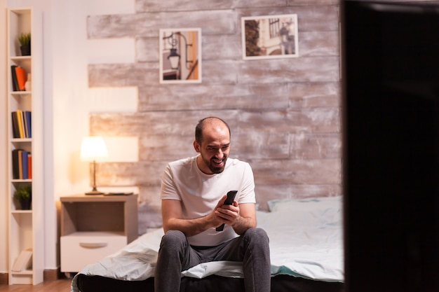 Homme de nuit en pyjama riant en regardant un film à la télévision.