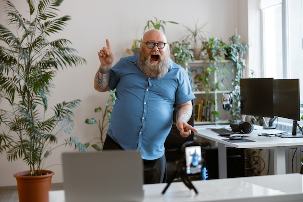 Un homme obèse barbu drôle danse en enregistrant une nouvelle vidéo pour un blog avec un téléphone à la maison