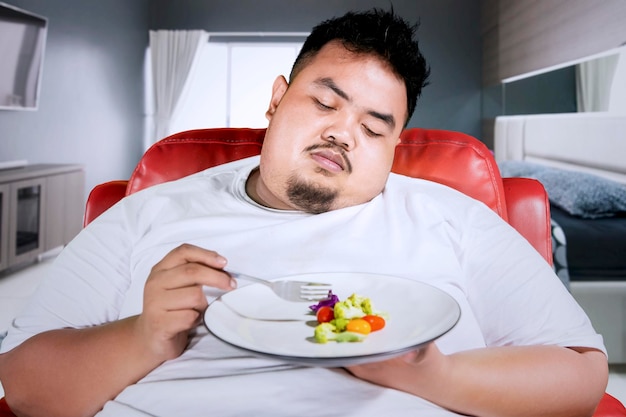 Photo un homme obèse triste mange de la salade dans la chambre