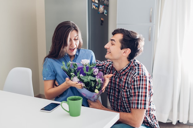 Homme offrant un bouquet de fleurs à sa petite amie dans la cuisine à la maison. Surprise romantique Saint Valentin