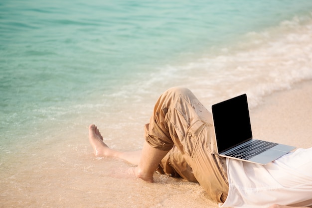 homme avec ordinateur sur la plage. travaillant sur ordinateur en plein air pendant le voyage, concept de pigiste.