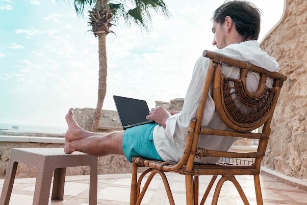 Homme avec un ordinateur portable dans ses mains se reposant et travaillant comme pigiste en vacances