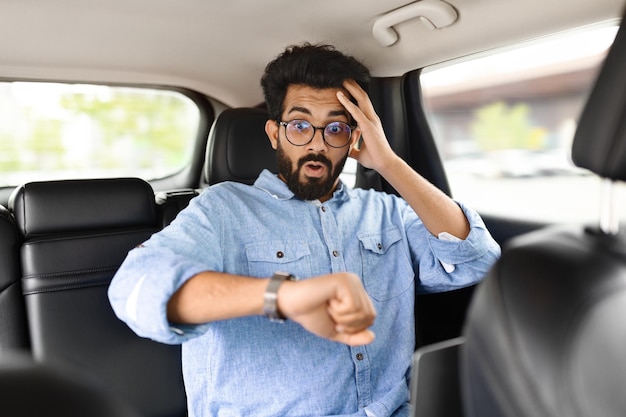 Homme oriental stressé regardant la montre toucher la tête dans la voiture