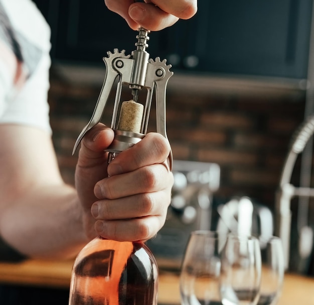 Homme ouvrant une bouteille de vin et des verres sur la table à la cuisine