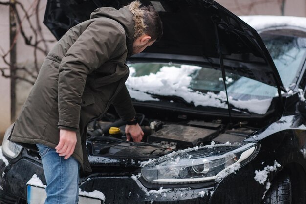 L'homme ouvre le capot de la voiture et essaie de trouver ce qui s'est passé avec l'homme de la voiture gratte l'arrière de