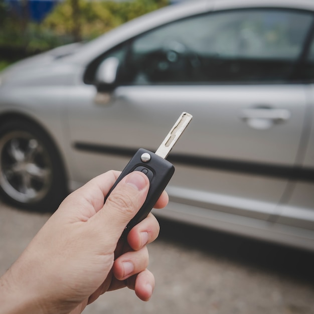 L'homme ouvre sa porte de voiture avec la télécommande de contrôle. La main masculine appuie sur le système d'alarme de la télécommande du véhicule sur fond de voiture garée. Désactivation de l'alarme automobile. Gros plan sur la clé du véhicule.