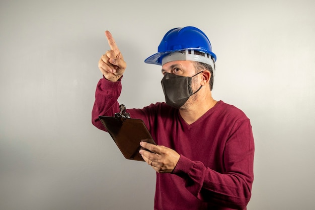 Homme d'ouvrier d'industrie civile avec le casque bleu et le presse-papiers à la main pointant vers le haut