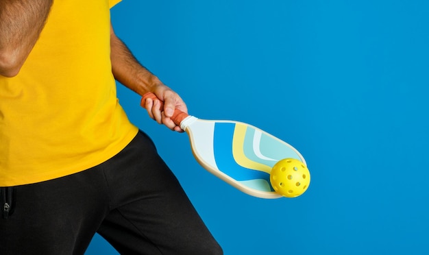 un homme avec une pagaie bleue en main et une balle jaune sur un fond bleu
