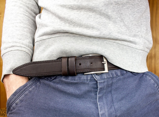 Un homme en pantalon avec une ceinture gros plan Un jeune homme mince dans un sweat à capuche blanc et un jean avec une ceinture gros plan anonyme