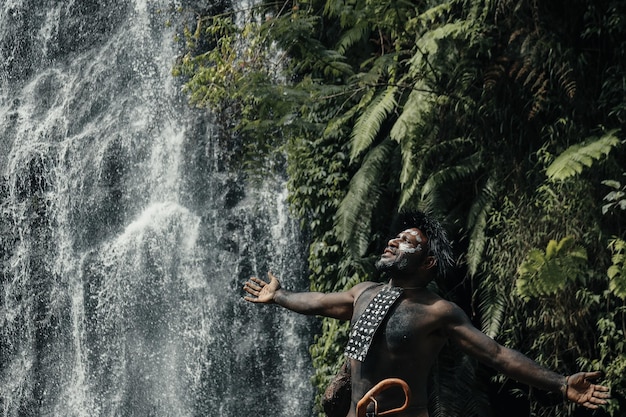 L'homme de Papouasie de la tribu Dani étendit ses mains pour ressentir la liberté contre la chute d'eau dans la forêt verdoyante