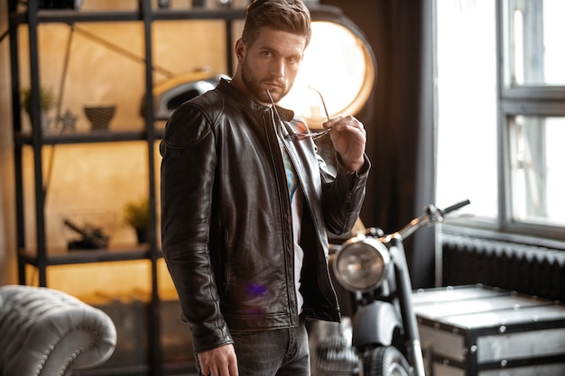 Homme parfait. Jeune hipster en blouson de cuir debout dans la chambre.