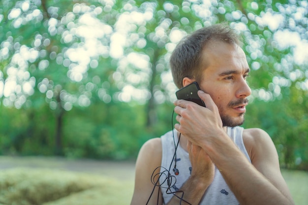 Un homme parlant au téléphone debout dans le parc Hipster barbu utilise un smartphone