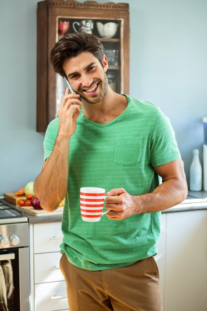 Homme parlant au téléphone et tenant une tasse de café dans la cuisine