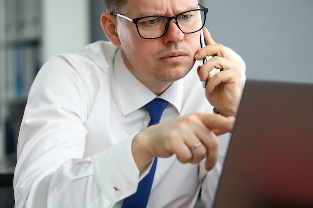 L'homme parle au téléphone et pointe vers l'écran de l'ordinateur.