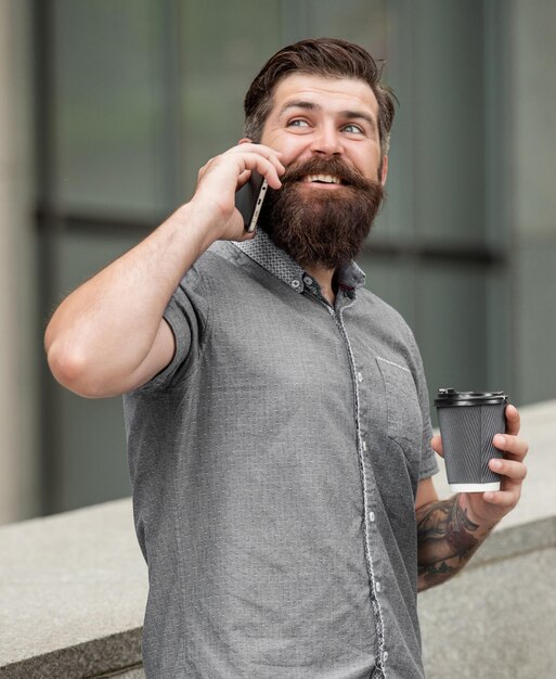 un homme parle sur un smartphone dans la rue avec un café photo d'un homme parle sur un smartphone un homme parle sur un smartphone à l'extérieur un homme parle sur un smartphone à l'extérieur