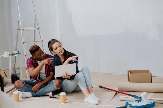 Un homme à la peau foncée et une belle femme sont assis sur le sol d'un appartement rénové