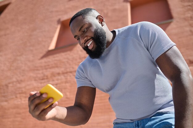 Un homme à la peau foncée vêtu d'un t-shirt blanc faisant un selfie