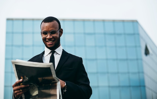 Un homme à la peau noire lit le papier devant le bâtiment du miroir. Homme d'affaires en pause