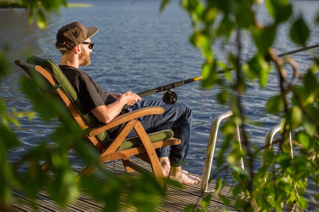 Homme pêchant depuis une jetée en bois près d'un chalet sur un lac en Finlande en été