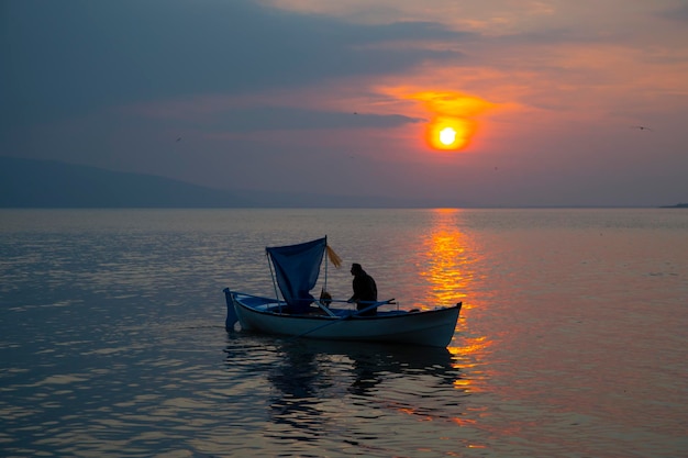 un homme pêche dans un bateau avec un soleil couchant derrière lui
