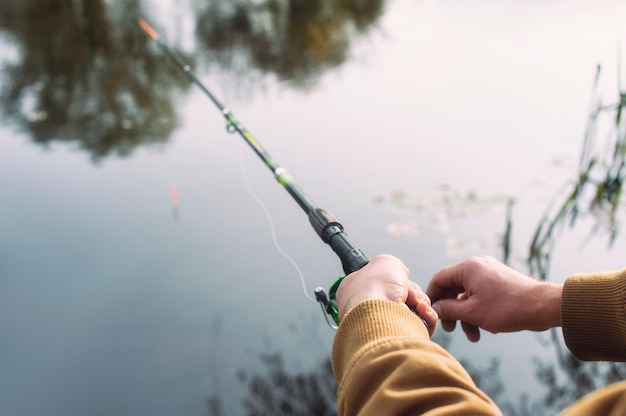 Homme pêcheur attrape un poisson sur une canne à pêche avec un moulinet sur le lac dans le contexte.