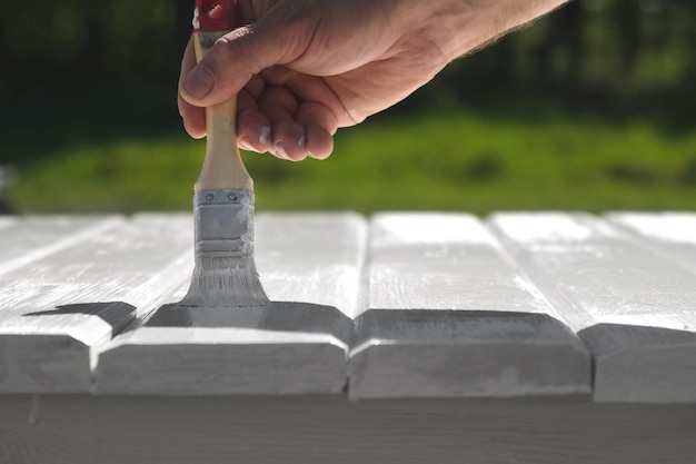 Homme peignant une table en bois à l'extérieur Rénovation de meubles de jardin Gros plan main avec un pinceau Amélioration de l'habitat Bricoleur vernissant des planches de bois à l'extérieur Peindre une surface en bois avec un colorant blanc