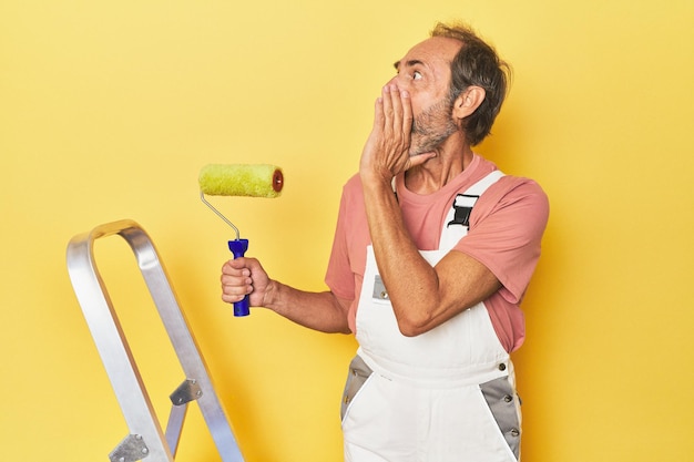 Homme peignant une toile de fond jaune en studio criant et tenant la paume près de la bouche ouverte