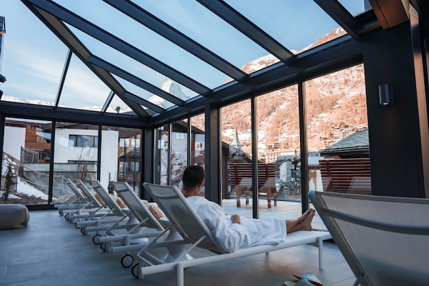 Homme en peignoir relaxant sur une chaise longue près de la fenêtre d'un hôtel de luxe