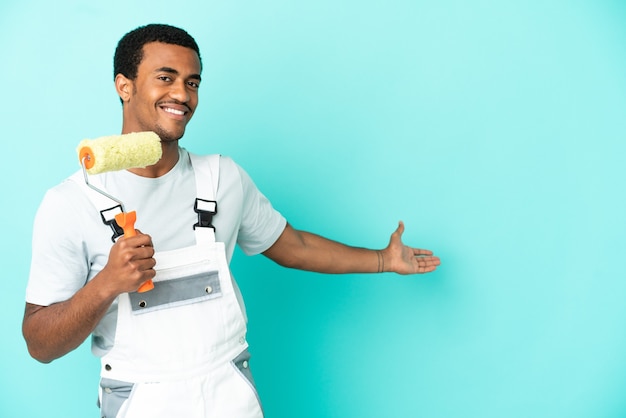 Homme peintre afro-américain sur fond bleu isolé tendant les mains sur le côté pour inviter à venir