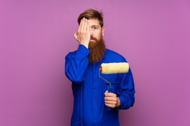 Homme peintre avec une longue barbe sur fond violet isolé couvrant un œil à la main