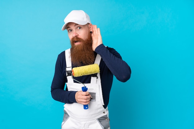 Homme peintre avec longue barbe sur mur bleu isolé écouter quelque chose