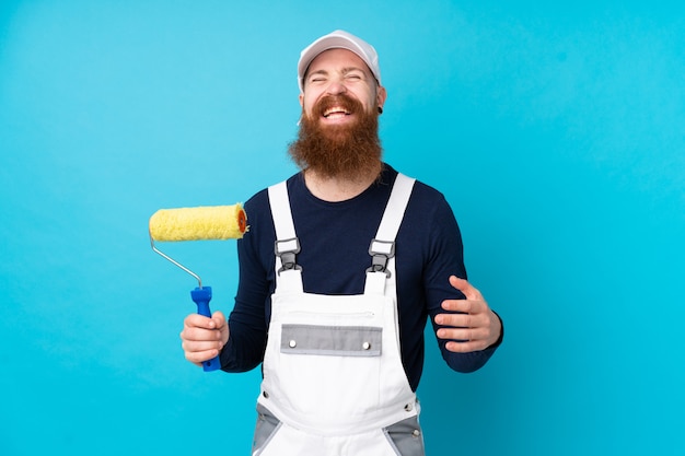 Homme peintre avec longue barbe sur mur bleu isolé en riant