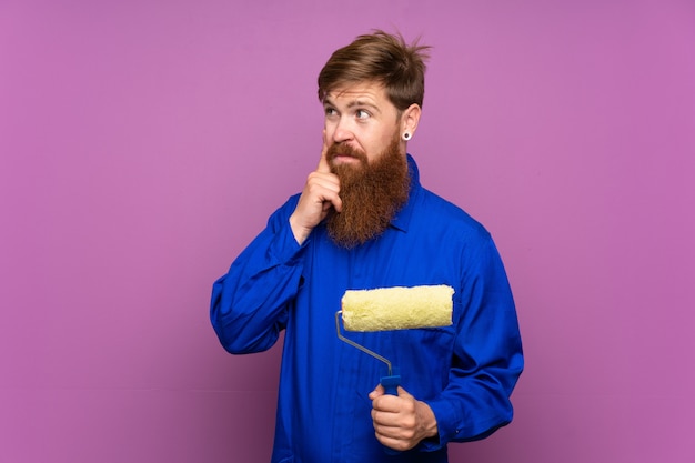 Homme peintre avec une longue barbe sur un mur violet isolé, pensant à une idée
