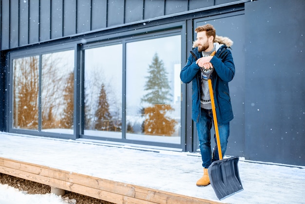 Homme avec pelle à neige près de la maison dans les montagnes