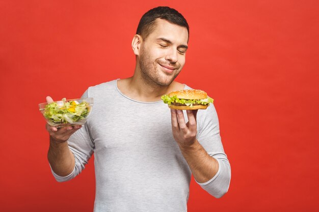 Homme pensant choisir entre salade et hamburger, nourriture saine et malbouffe